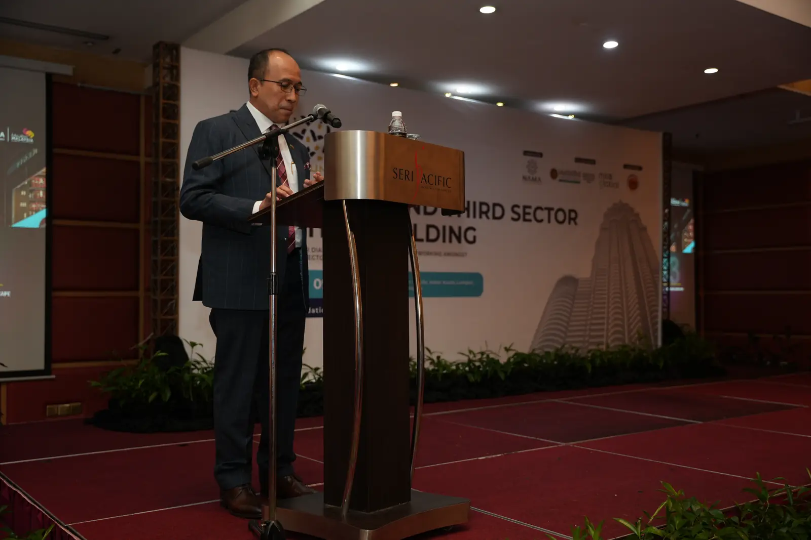 A speaker at the podium in front of the event backdrop